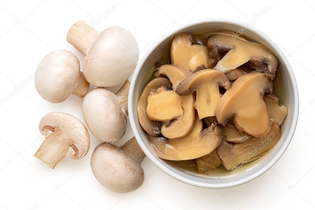 Canned sliced button mushrooms in a white ceramic bowl next to fresh button mushrooms isolated on white. Top view.