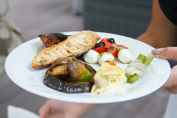 Main tenant une assiette avec saumon grillé et salade, à l'extérieur . — Photo