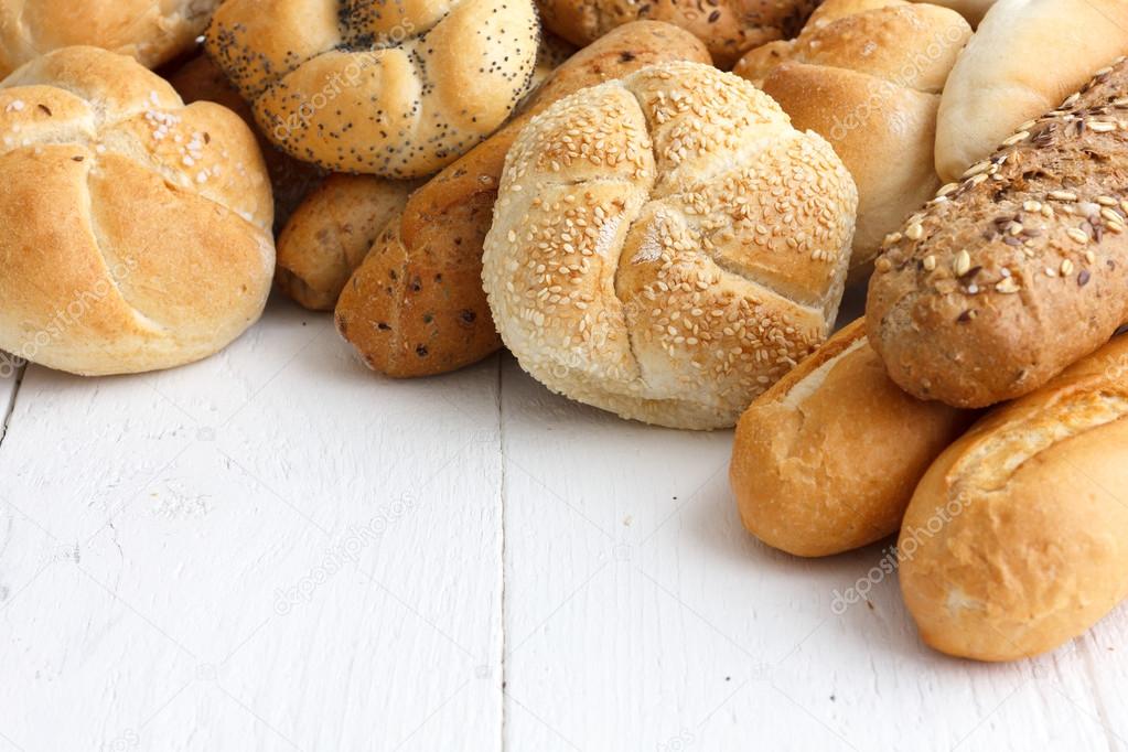 Many types of bread rolls on white wood.