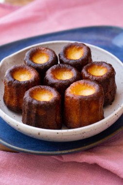 Pembe masa örtüsü üzerinde küçük bir tabak Caneles de Bordeaux.