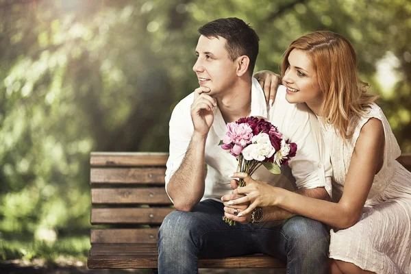 Joven pareja atractiva sentada en el banco en el parque y embraci — Foto de Stock