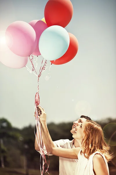 Joven feliz pareja sosteniendo coloridos globos y sonriendo — Foto de Stock