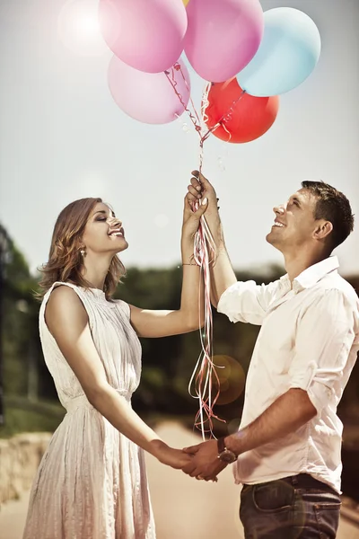 Jovem casal feliz segurando em suas mãos balões coloridos e s — Fotografia de Stock