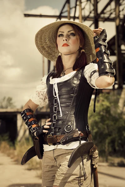 Young steampunk woman in leather corset and vietnam hat  standin