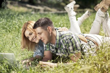 Happy young couple lying on the grass, looking at laptop and smi clipart