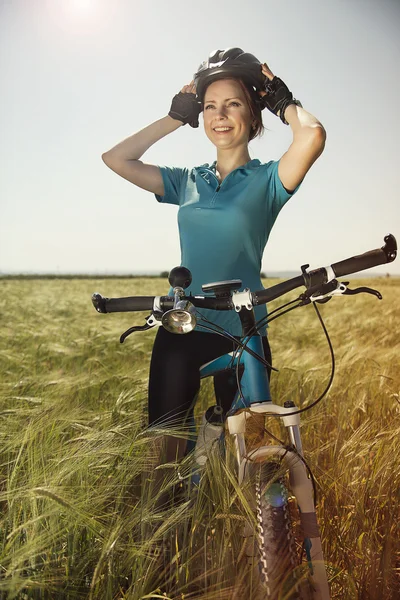 Happy beautiful young woman with a bike on a field holding her h — Stock Photo, Image