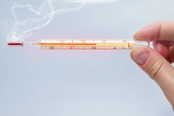 Heat mercury thermometer in the hand of a man isolated on a blue background. High temperature concept, Temperature measurement using a thermometer. High fever and illness. Close up