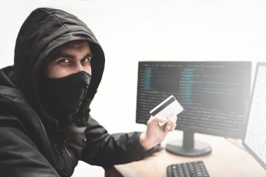 Elinde çalıntı kredi kartıyla beyaz arka plandaki kurnaz bilgisayar korsanı banka hesabından para çalmaya çalışıyor. İnternet hırsızlığı kavramı