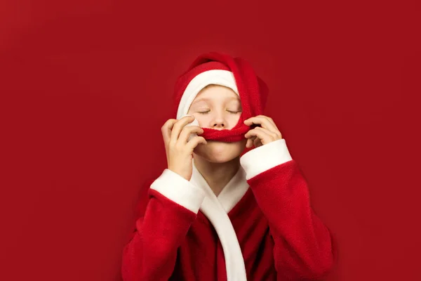 Um menino de traje de Papai Noel brinca com seu chapéu — Fotografia de Stock