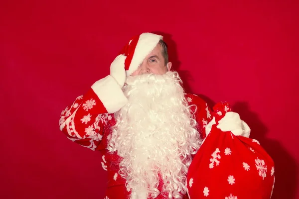 Fatigué Père Noël enlève son chapeau, l'autre main tient un sac de cadeaux, sur un fond rouge. — Photo