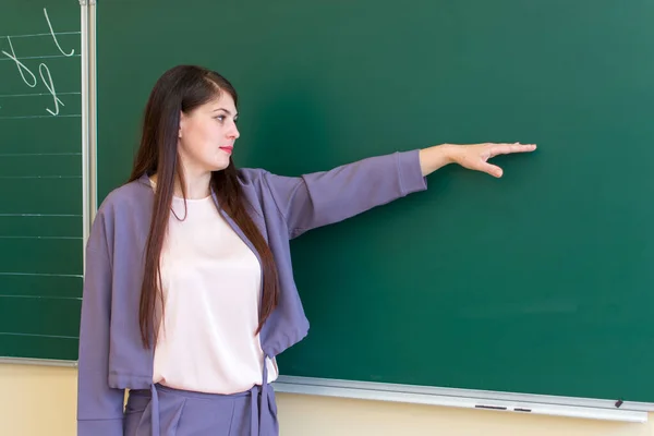 Leraar basisschool geeft les aan kinderen, wijst naar het schoolbord. — Stockfoto