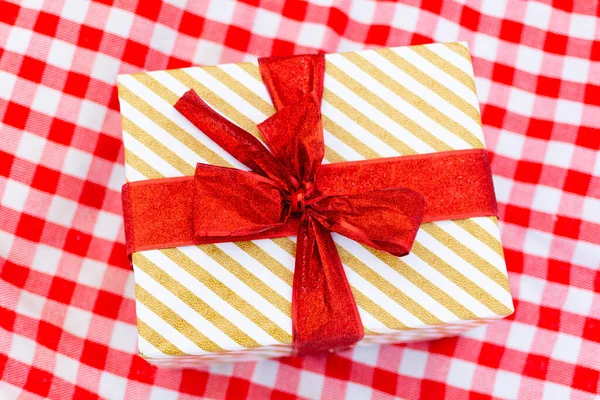 Una confezione regalo con fiocco rosso, stesa sulla tovaglia. — Foto Stock