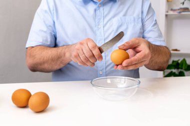 Mavi gömlekli bir adam, saydam bir fincana bıçakla yumurta kırıyor..