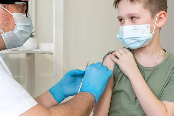 Um médico masculino em uma máscara protetora e com um estetoscópio vacina uma criança. — Fotografia de Stock