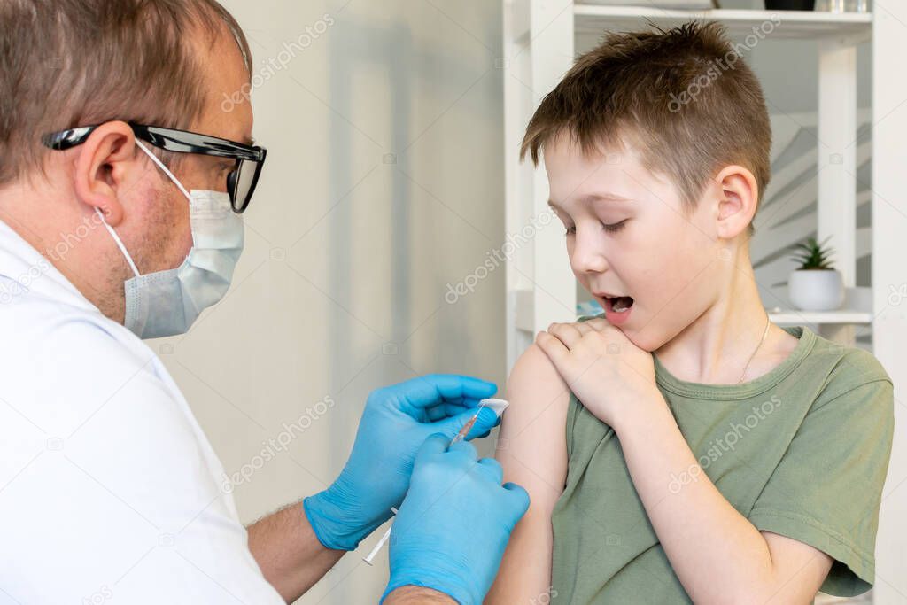 A male doctor in a protective mask and with a stethoscope vaccinates a child.