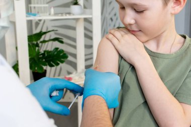 Koruyucu maskeli ve steteskoplu bir erkek doktor bir çocuğu aşılıyor..