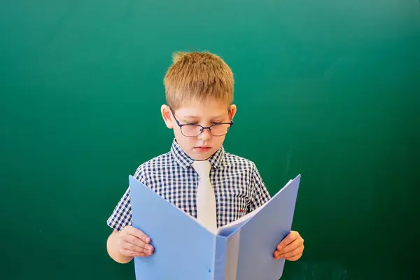 Een student leest een boek terwijl hij bij het groene schoolbord staat — Stockfoto