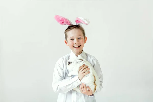 Niño con orejas de conejo sosteniendo un conejo blanco. — Foto de Stock