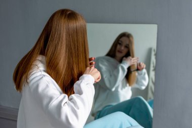 Genç bir kadın uzun saçlarını tarıyor. Aynadaki yansımadan bak..