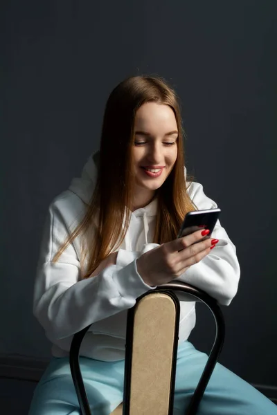 長い髪の若い女性が椅子に座って携帯電話を手に. — ストック写真