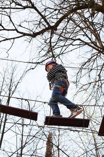 A child in a rope adventure park. The boy climbs a high rope path. Dexterity skills — Stock Photo, Image