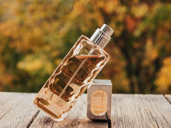Sales and beauty business concept. Perfume in a glass bottle on a autumn blurred background. Toilet water, still life. Flat lay composition, decoration design. Vertical view, soft focus.