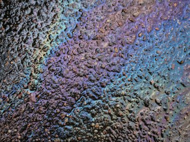 Petrol ürünlerinin yağ lekeleriyle soyut bir arkaplan. Çok renkli grunge dokusu. Islak asfalt yolda benzin lekeleri var. Ekoloji ve çevre kirliliği kavramı.