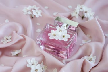 Kapatın cam şişe aromatik lüks parfüm. Yumuşak pembe ipek kumaş ve filizlenmiş çiçekler. Minimalist ambalaj, markalaşma. Çiçek kokusu. Şeffaf cam kolonya aroması şablonu.