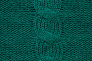 Wool hand-knitted or machine knitting pattern with braids. Knit warm green sweater or scarf. Cozy dark emerald blanket background. Fabric texture close up. Comfortable style cloth. 