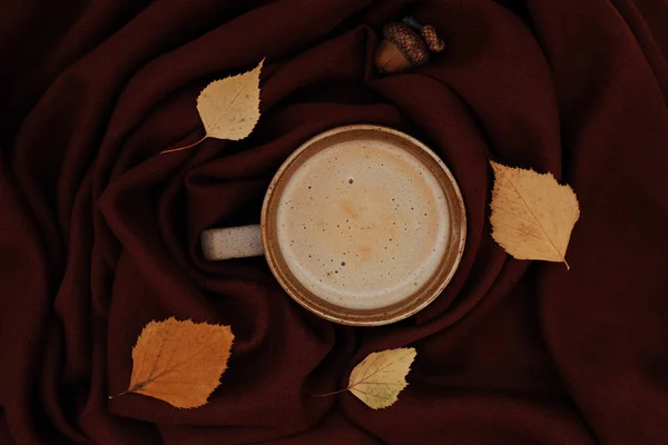 Atmosferico caffè autunnale o autunnale mattutino dai colori caldi. Foglie giallo autunno, ghianda, tazza calda di caffè nero e accogliente sciarpa marrone come sfondo. Domenica rilassante, umore autunnale e concetto di natura morta. — Foto Stock