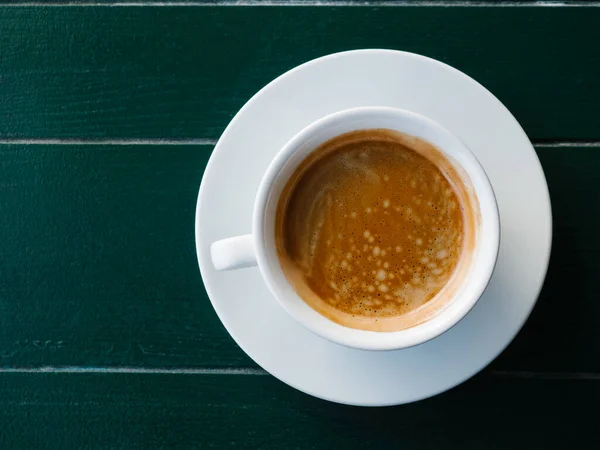 Una tazza di caffè nero con schiuma su uno sfondo di legno smeraldo, vista dall'alto. Espresso o americano. Caffè e bar, concetto di arte barista. Minimalismo. — Foto Stock