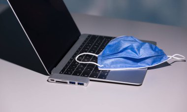 Dizüstü bilgisayarda covid 19 Coronavirus 'a karşı koruyucu maske, USB' nin USB-C adaptörü, beyaz masa, merkez ofisin, ciddi akciğer hasarına yol açabilecek tehlikeli bulaşıcı hastalığı azaltmak için dünya çapında tavsiye edilmektedir.