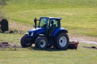 Mavi traktör saha çalışması için hazır ama sürücüsüz yeşil çayırda, ön taraftan, insanların olmadığı bir günde.