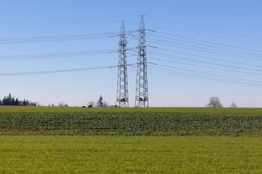 Bulutsuz mavi gökyüzünün altındaki yeşil bir tepenin arkasında büyük çelik elektrik direkleri. Güç üretimi, gün boyunca insan olmadan çok fazla enerjiye ihtiyaç duyar.