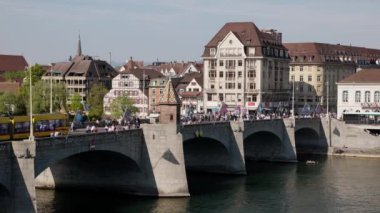 Basel İsviçre, 24 Nisan. 2021: Ren Köprüsü Basel, eski kasabadan çekilen, köprüden geçen sarı ve yeşil tramvay, öğleden sonra birçok insan şehirde, işten geliyor ya da alışverişe gidiyor.