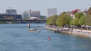 Basel İsviçre, 24 Nisan. 2021: Ren mavisi yolcu feribotunun önü yaz günü birçok insan kıyıda oturup arka plandaki güzel hava endüstrisinin tadını çıkarıyor. 
