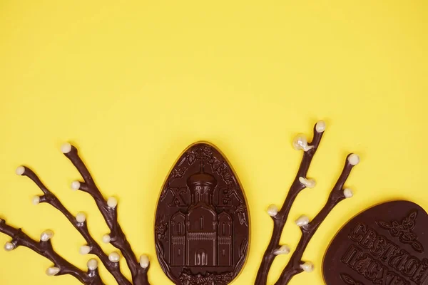 Chocolate eggs and chocolate willow on a yellow background. Place for the test. Postcard or banner concept.
