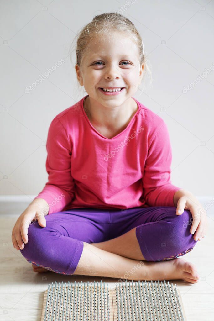 Little beautiful yogini girl in a pink sweater. Sadhu's board for children. Children's yoga. Baby sitting in lotus position