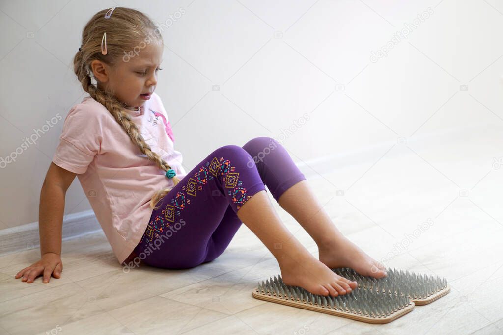 Little beautiful yogini girl. Stands on the board of a sadhu. Practicing yoga. The girl stands on the nails.