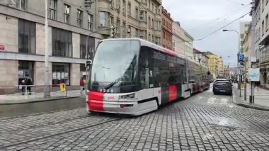 Prag 'daki kaldırım taşı meydanından geçen iki modern kırmızı ve beyaz tramvay, yayaların yakınına taşınması ve konut binalarının caddelerde sıralanması, günlük şehir hayatını ve toplu taşımayı gösteriyor. Sadece editör kullanımı.