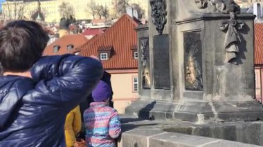 Prag, Çek Cumhuriyeti 24 Şubat 2026: Parlak bir kış günü öğleden sonra Charles Köprüsü 'nü geçen bir turist topluluğu, kaldırım kaldırımının üzerindeki süslü kaidelerin üzerinde duran büyük Barok taş heykellerinin her iki tarafında da yer aldı..