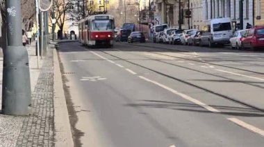 Prag, Çek Cumhuriyeti 24 Şubat 2026: Etkileyici bir kış sabahı, gösterişli neoklasik taş cephesi olan Vltava seti üzerindeki görkemli Ulusal Tiyatrosu 'nun önünden uzun, kırmızı ve beyaz bir tramvay geçiyor