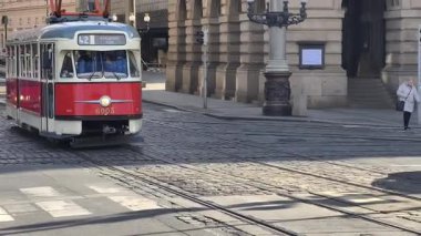 Prag, Çek Cumhuriyeti 24 Şubat 2026: Etkileyici bir kış sabahı, gösterişli neoklasik taş cephesi olan Vltava seti üzerindeki görkemli Ulusal Tiyatrosu 'nun önünden uzun, kırmızı ve beyaz bir tramvay geçiyor