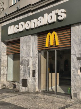 Prag, Çek Cumhuriyeti 6 Mart 2026: Cam girişi ve modern tabelası olan bir fast food restoranının dış görünüşü. Yayalar restoranın önündeki kaldırım taşı boyunca yürürken, tabela açıkça McDonalds olarak tanımlıyor.