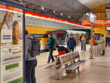 Prag, Çek Cumhuriyeti, 9 Mart 2026 Yolcular, bir metro treni modern yeraltı istasyonuna vardığında platformda yürümek ve beklemek, kıvrımlı tavanlar, parlak ışıklandırma, redandwhite tabelası ve günlük banliyö aktivitesi.