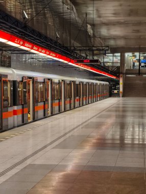 Prag, Çek Cumhuriyeti, 9 Mart 2026 Yolcular, bir metro treni modern yeraltı istasyonuna vardığında platformda yürümek ve beklemek, kıvrımlı tavanlar, parlak ışıklandırma, redandwhite tabelası ve günlük banliyö aktivitesi.