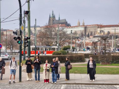 Prag, Çek Cumhuriyeti, 11 Mart 2026, Vltava nehri yakınlarındaki tarihi merkezde günlük yaşam ve ulaşım altyapısı. Yaya geçitlerinden geçen tramvaylar, yolcular ve yayaların yer aldığı şehrin gazetecilik manzarası.