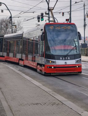 Prag, Çek Cumhuriyeti, 11 Mart 2026, Vltava nehri yakınlarındaki tarihi merkezde günlük yaşam ve ulaşım altyapısı. Yaya geçitlerinden geçen tramvaylar, yolcular ve yayaların yer aldığı şehrin gazetecilik manzarası.