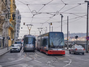 Prag, Çek Cumhuriyeti, 11 Mart 2026, Vltava nehri yakınlarındaki tarihi merkezde günlük yaşam ve ulaşım altyapısı. Yaya geçitlerinden geçen tramvaylar, yolcular ve yayaların yer aldığı şehrin gazetecilik manzarası.
