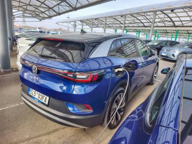 Prag, Çek Cumhuriyeti - 14 Mart 2026: Güneşli bir günde halka açık bir otoparkta şarj istasyonlarına bağlı modern elektrikli araçlar. Bir EV şarj sürecinin arabalara bağlı kablolar ve prizlerle gazetecilerin yakın plan görüntüsü.